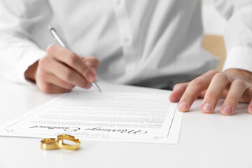 Man signing marriage contract and wedding rings on desk, selective focus