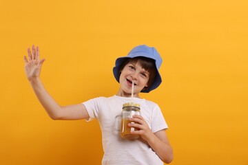 Happy little boy in panama hat with mason jar of juice on orange background. Refreshing drink