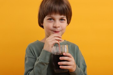 Cute little boy drinking refreshing soda on orange background