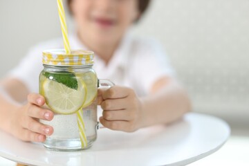 Fototapeta premium Little boy with mason jar of lemonade at table indoors, selective focus. Refreshing drink