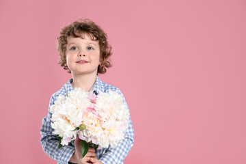 Cute little boy with bouquet of beautiful peonies on pink background. Space for text