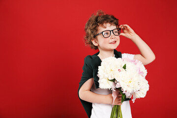Cute little boy with bouquet of beautiful peonies on red background. Space for text