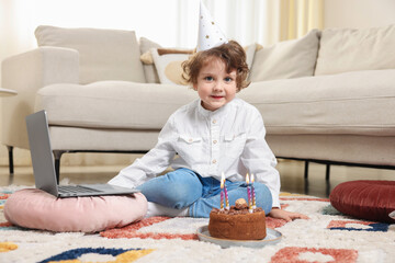 Birthday celebration. Little boy with cake having video call via laptop at home