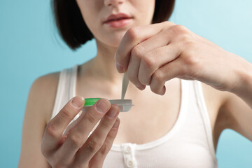 Woman taking contact lens out of case on light blue background, closeup
