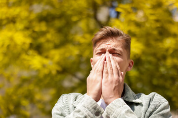 Young man suffering from seasonal pollen allergy near tree on spring day. Space for text