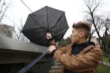 Man with broken umbrella fighting wind under rain outdoors