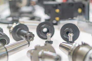 Close-up of scattered metallic mechanical parts on a light grey surface, possible industrial setting Variable shapes gears, rings, rods, sizes, and angles Overhead lighting casting soft shadows a