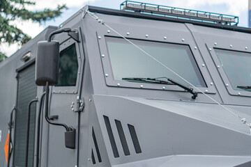 Gray armored personnel carrier APC under overcast skies, angular shape, multiple windows, tinted or protected, antenna, rugged terrain design, side perspective, no visible texts or branding, open a