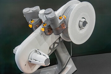 White and black robotic device with central cylinder, yellow figurines, indoor setting, technical exhibit or convention