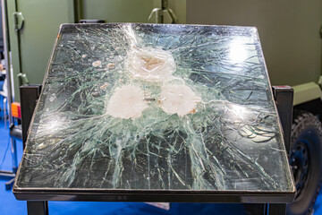 Rectangular glass object, shattered into jagged pieces like a sunburst, possibly in an indoor workshop or storage setting No texts visible, side perspective emphasizing depth and extent of damage A