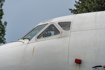 An aged white single-engine aircraft, parked outdoors on an overcast day with open cockpit windows The wing extends to the left and theres a small red anti-collision light at the tip Natural setti
