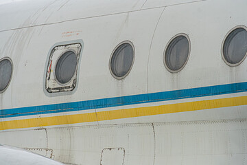 Large white and blue-orange striped jet airplane on airport tarmac, visible engines, open front door revealing interior lighting, no identifying marks