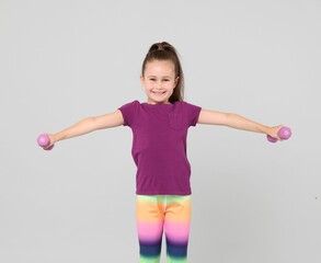Little girl with dumbbells on light grey background