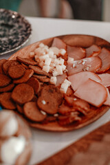 A table covered with various foods, a meat, cheese, crackers on th plate in the center