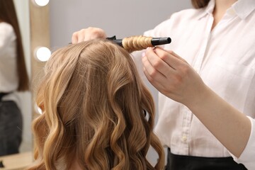 Fototapeta premium Hairdresser curling woman's hair in salon, closeup
