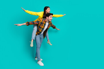 Young happy couple having fun with piggyback ride against teal background, showcasing playful bonding and joy