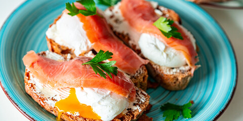 Poached eggs with salmon on bread toast with cream cheese on a turquoise plate. Close-up. A...