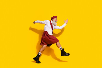 Cheerful senior man wearing traditional Scottish attire jumping against a vibrant yellow background, expressing happiness