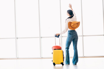 Cheerful female traveler with suitcase in airport terminal waving, ready for a new destination and...