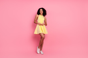 Young woman in a vibrant yellow dress posing against a pink background, showcasing style and...