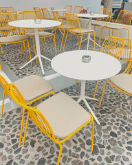 Cozy cafe in an unusual Santorini style with yellow metal chairs and white round tables
