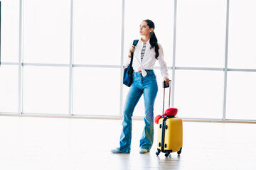 Young woman in casual attire with luggage at a modern airport terminal, ready for travel and...