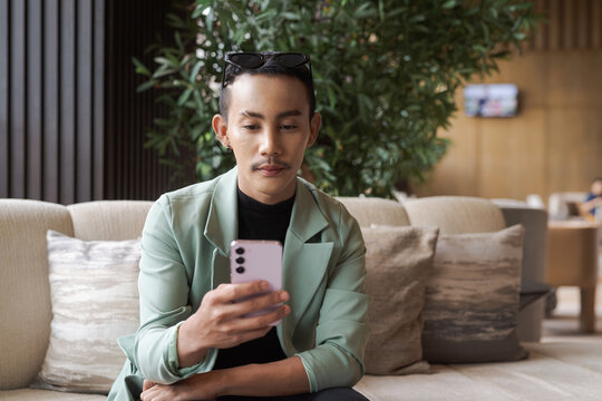 Portrait of nonbinary genderfluid young Asian gay businessman using phone in cafe
