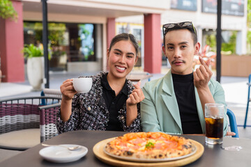 Happy friends eating pizza together and making mini heart gesture