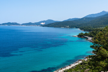 Scenic coastal landscape with crystal clear blue water and forested mountains in Greece. Aegean Costline with turquoise water and green hills. 