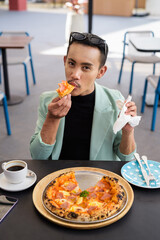 Portrait of nonbinary genderfluid young Asian gay man eating pizza ourdoors