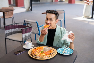 Portrait of nonbinary genderfluid young Asian gay man eating pizza ourdoors