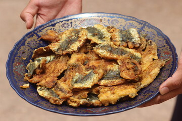 Hands holding a plate with fried sardines