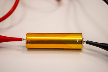 Close-up image of a battery connected with alligator clips, isolated on a white background.