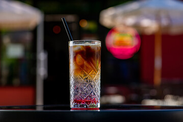 Espresso tonic cocktail in a glass glass with a straw on a table on a summer terrace in a cafe