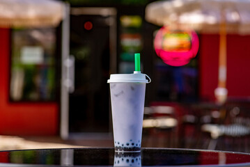 Bubble tea in a tall glass with a straw to go on a table on a summer terrace in a cafe