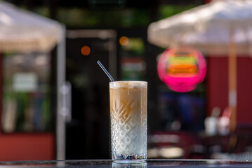 White Milky shake with coffee in a tall glass with a straw on a table on a summer terrace in a cafe