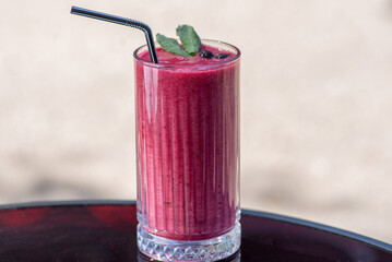 Berry smoothie in a tall glass with straw