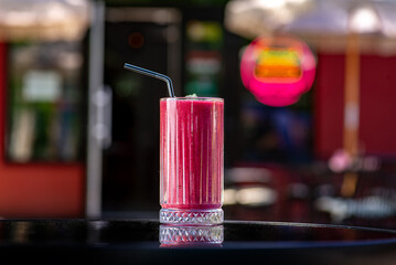 Berry smoothie in a tall glass with straw on a table on a summer terrace in a cafe