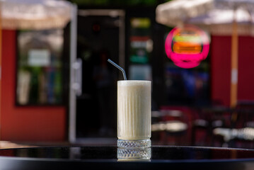 Yellow White Milky shake in a tall glass with a straw on a table on a summer terrace in a cafe