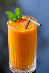 Orange fruity smoothie in a tall glass with straw