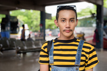 Portrait of nonbinary genderfluid young Asian gay tourist man in bus terminal