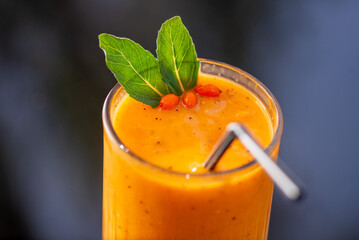 Orange fruity smoothie in a tall glass with straw