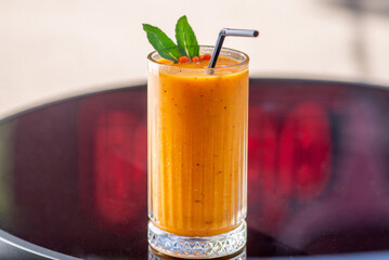 Orange fruity smoothie in a tall glass with straw