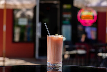 Banana Strawberry Smoothie in a tall glass with straw on a table on a summer terrace in a cafe