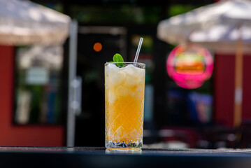 Orange lemonade in a tall glass with mint leaf and ice on a table on a summer terrace in a cafe