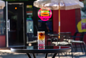 Espresso tonic cocktail in a glass glass with a straw on a table on a summer terrace in a cafe