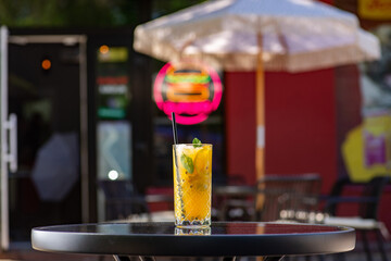 Orange lemonade in a tall glass with mint leaf and ice on a table on a summer terrace in a cafe