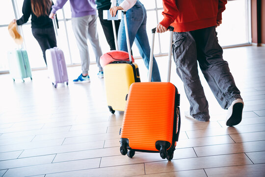 Group of young travelers walking with colorful luggage in an airport terminal on a bright day, preparing for a journey