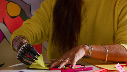 Artist with prosthetic hand arranging colorful sticky notes in art studio environment