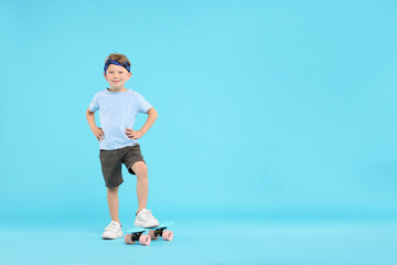 Little boy with penny board on light blue background, space for text